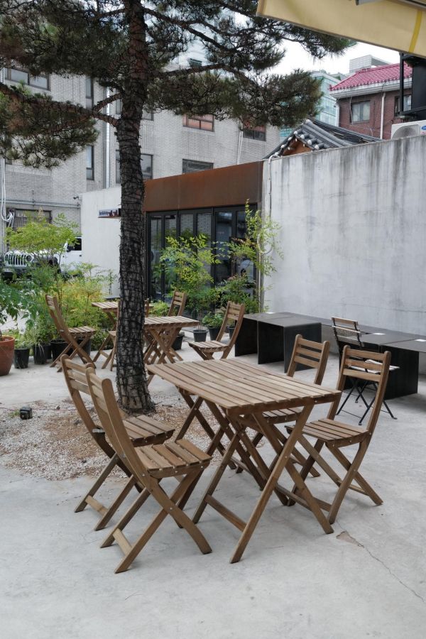 Small backyard gravel courtyard with stepping stones, wood bench, beige cushions, bright sunlight, and wood fence for small backyard ideas without grass.