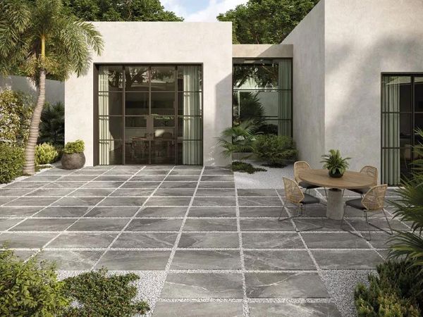Small backyard modern black courtyard with dark gravel, concrete slabs, sculptural tree, and ambient wall lighting