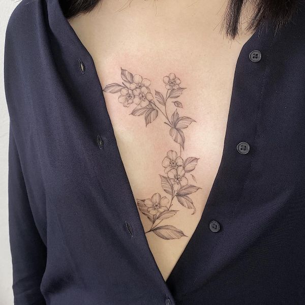 Subtle movement shot of sternum underboob tattoo with vine roses tracing under chest line, wrap style fine line black ink, sensual romantic feel.