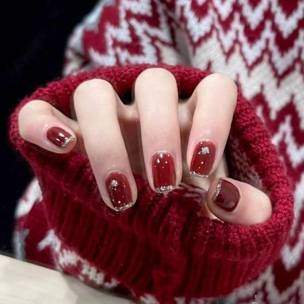 Elegant red nail designs for wedding celebrations with glossy burgundy nails and delicate gold glitter accents