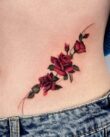 Red rose tattoo on waist with deep floral shading and soft curves