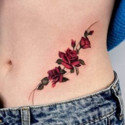 Red rose tattoo on waist with deep floral shading and soft curves