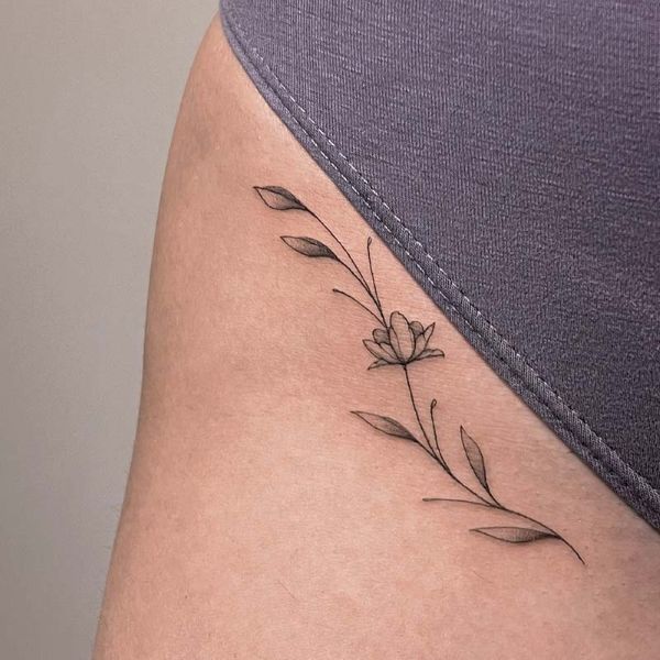Fine line floral waist tattoo with delicate leaves and soft black ink