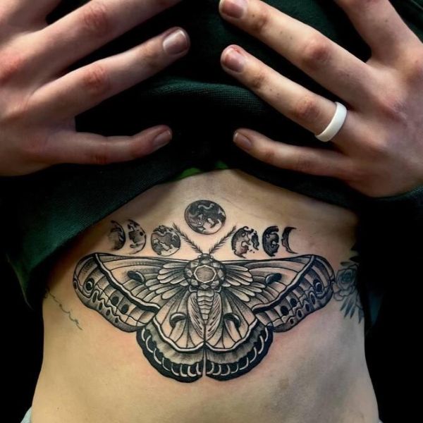 Moth underboob tattoo with moon phases and fine line wings following chest curve