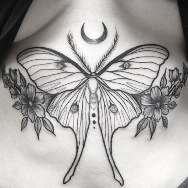 Moon and moth underboob tattoo with symmetrical wings, crescent moon above, and floral details