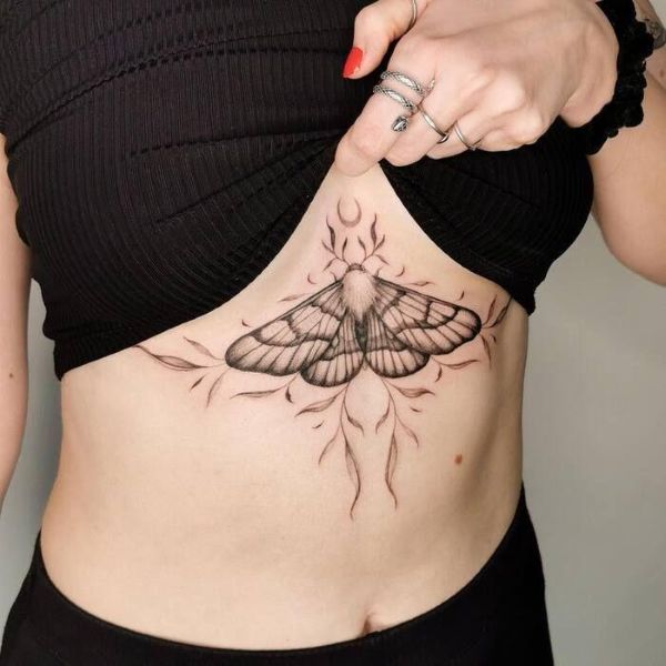 Shadow Drip Moth tattoo underboob with soft shading, flowing lines, and subtle flame-like details