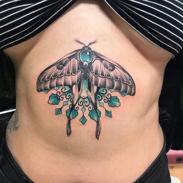 Botanical Frame Underboob Moth tattoo with soft color shading, teal accents, and ornamental leaf details