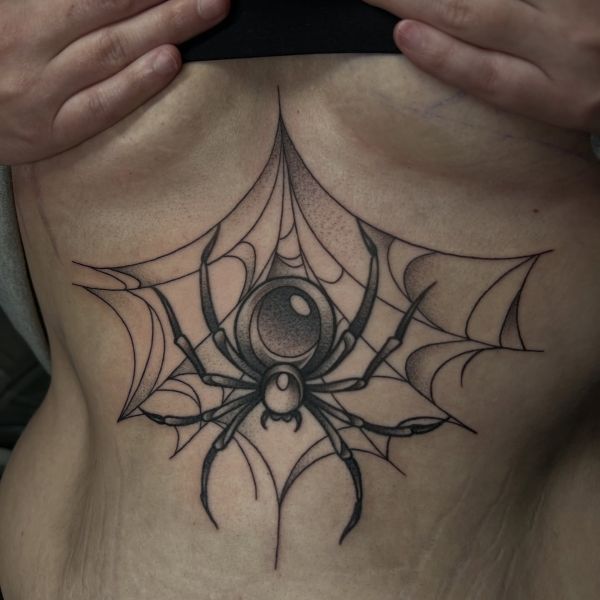 Ornamental spiderweb sternum tattoo with a bold spider centerpiece beneath the chest